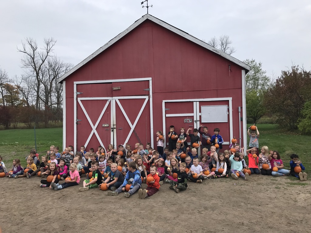 children sitting in from of red barn