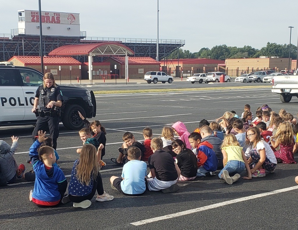 officer, police car and kids sitting and listening 