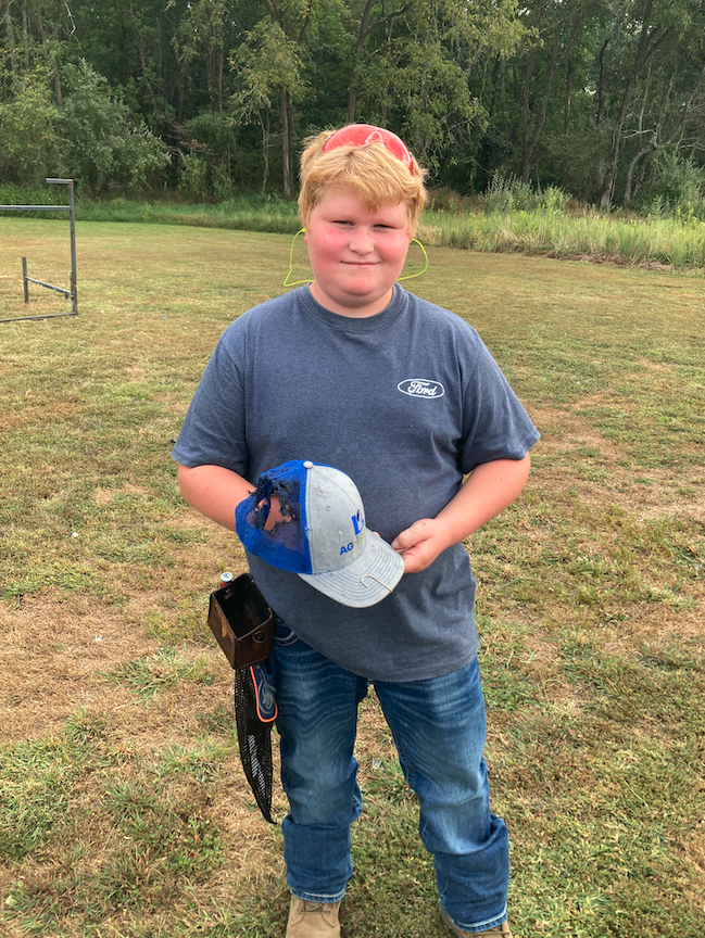 young male with blonde hair wearing a light blue ford t-shirt holding a hat with a hole in it