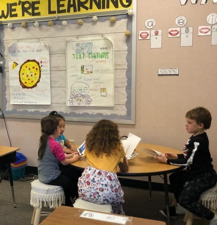 4 first graders work at a table on books