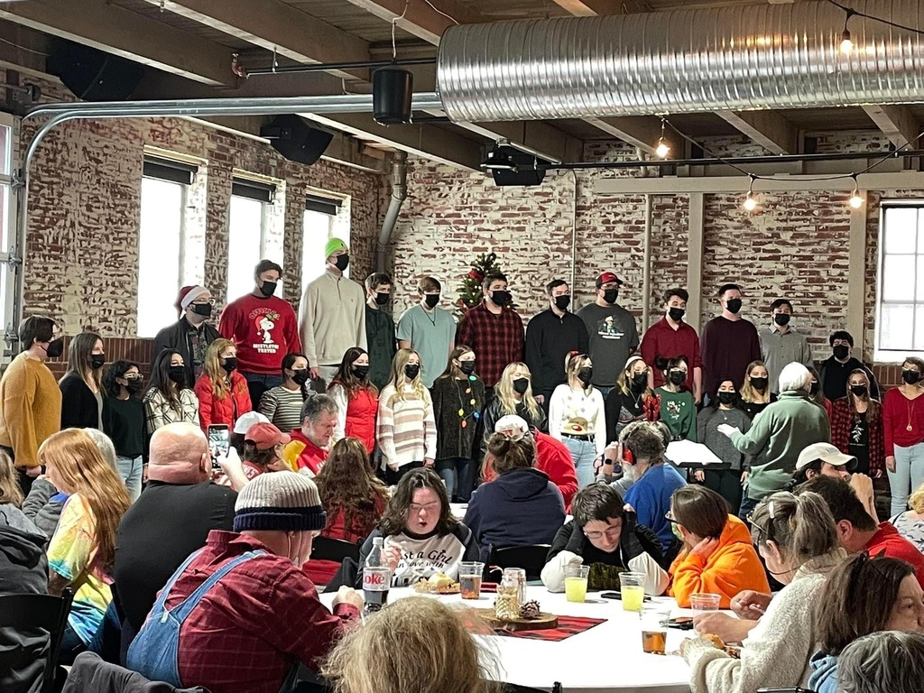 students singing to adults sitting at tables. 