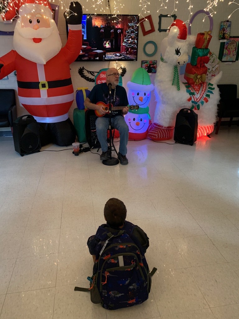 kindergarten student sitting on the floor listening to Mr. Mike sing Christmas carols