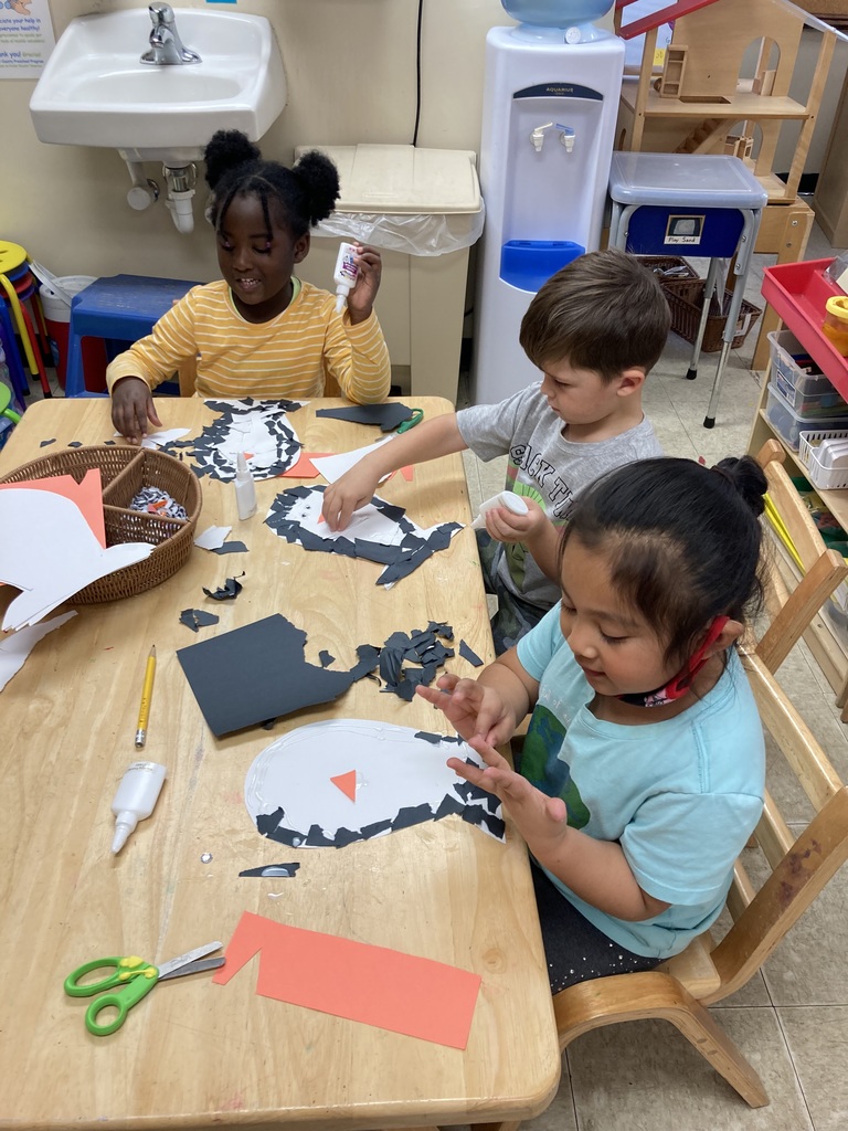 Three kids are tearing small pieces of black paper to make penguins in the Art Center.