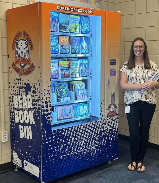 Mrs. Blundon is standing next to the new book vending machine .
