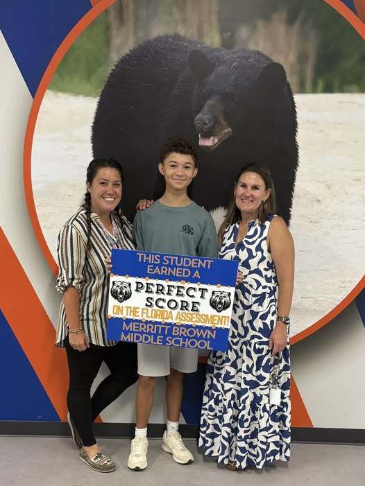 Easton holding a Perfect Score sign standing with Ms. Bufkin and Dr. Hart.