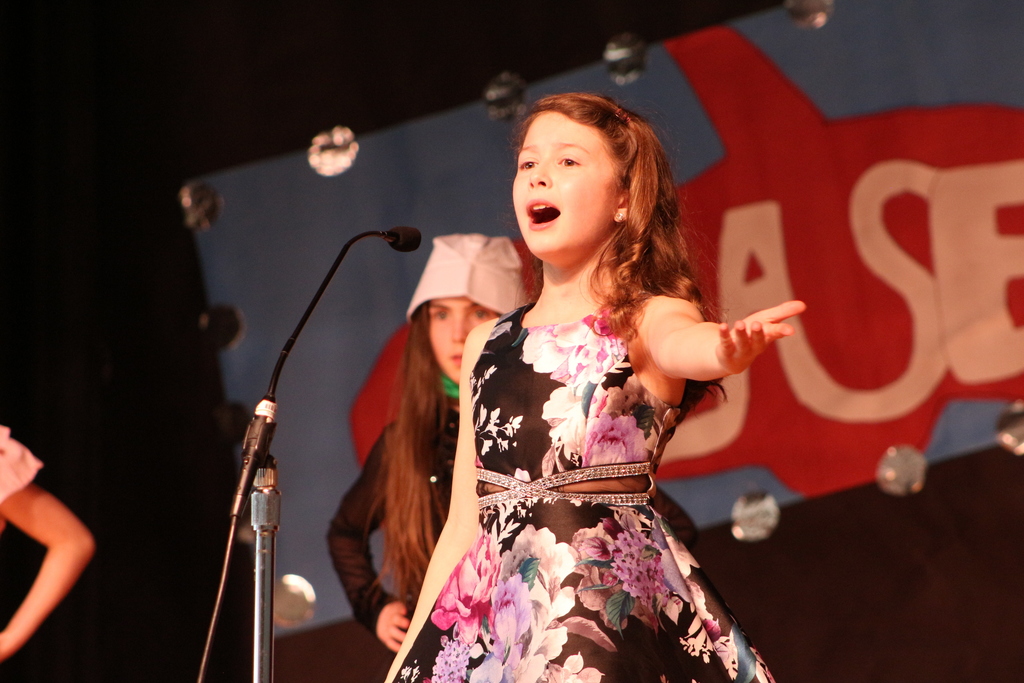 A girl holds out her hand and sings.