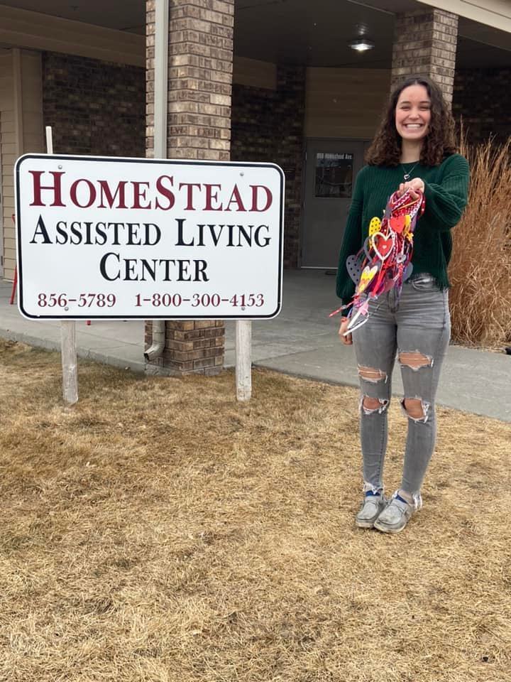 HomeStead Assisted Living Center, student standing outside by the sign holding door hangers