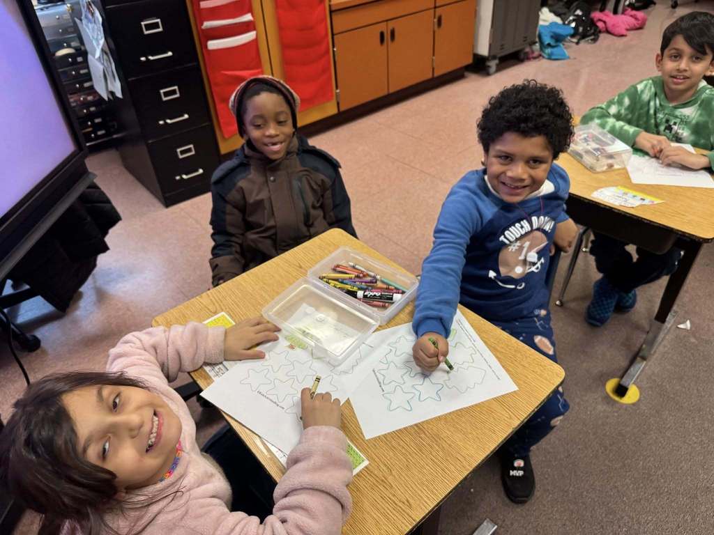 A group of students coloring and smiling at the camera.