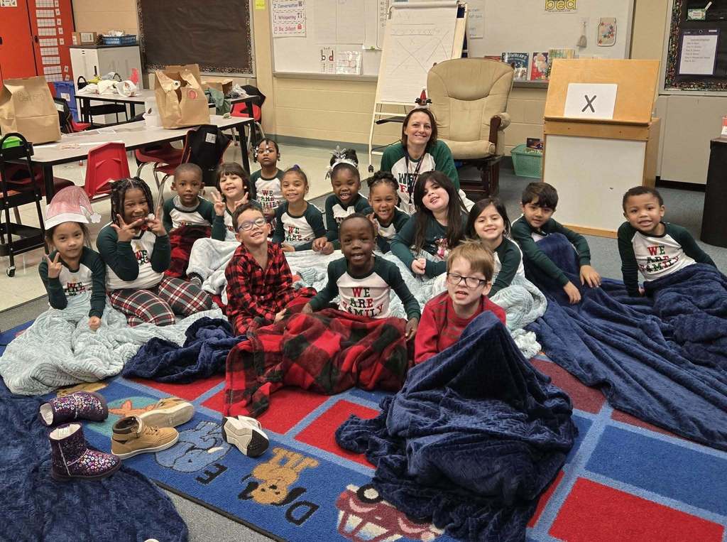 A group of students and teacher in pajamas and blankets smiling.