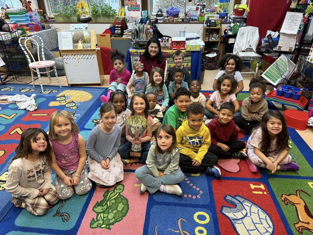 A group of kids smiling while sitting on the floor in a classroom. 