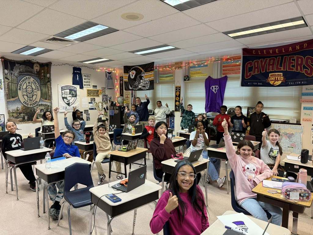 A group of kids smiling in a classroom, with their hands raised. 