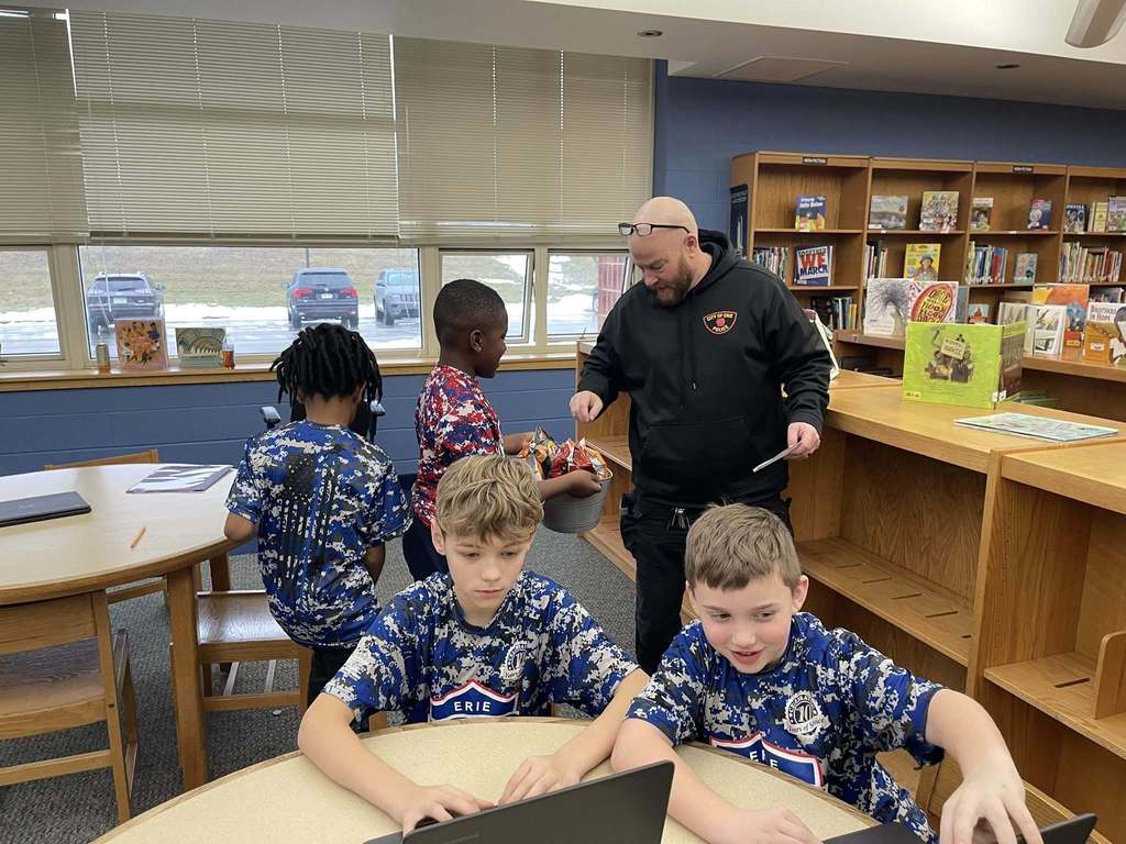 Students in a library and one student is offering snacks to a police officer. 