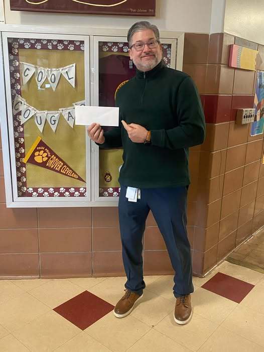 A man in a green sweater and jeans standing and smiling. 