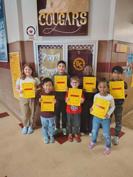 Students standing in a hall smiling and holding bright yellow paper. 