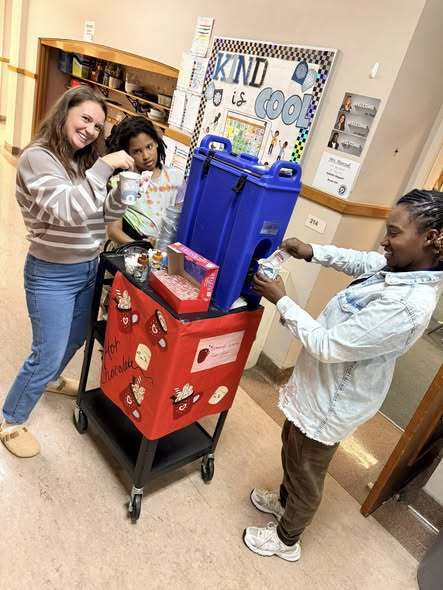 Adult and students at the cart filling cups of hot chocolate.