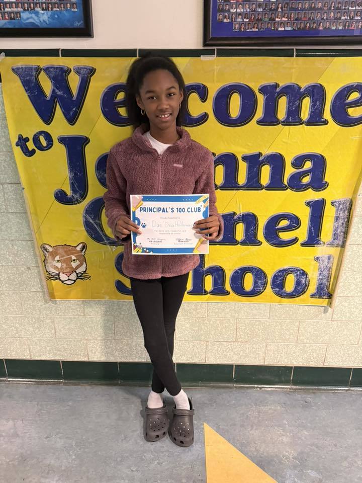 Young girl wearing a fluffy pink top and holding her certificate. 