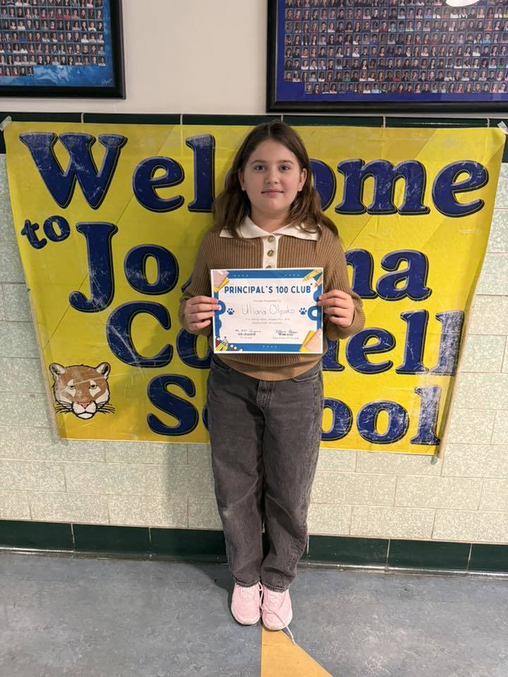 Young girl wearing a brown top and holding her certificate. 