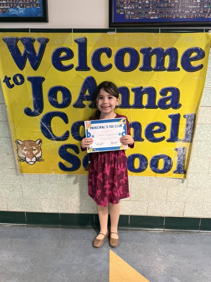 Young girl wearing a purple dress with bows on it while holding her certificate. 
