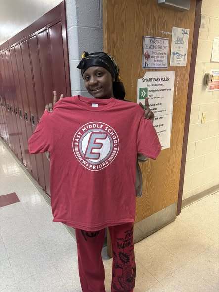 Young girl holding up a red shirt with the East Middle School logo on it. 