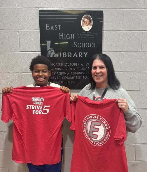 A student and teacher holding up a red shirt with the East Middle School logo on it. 