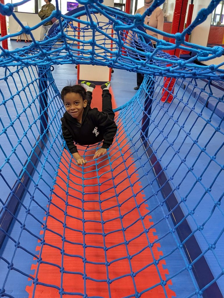 Young boy crawling through a net tunnel.