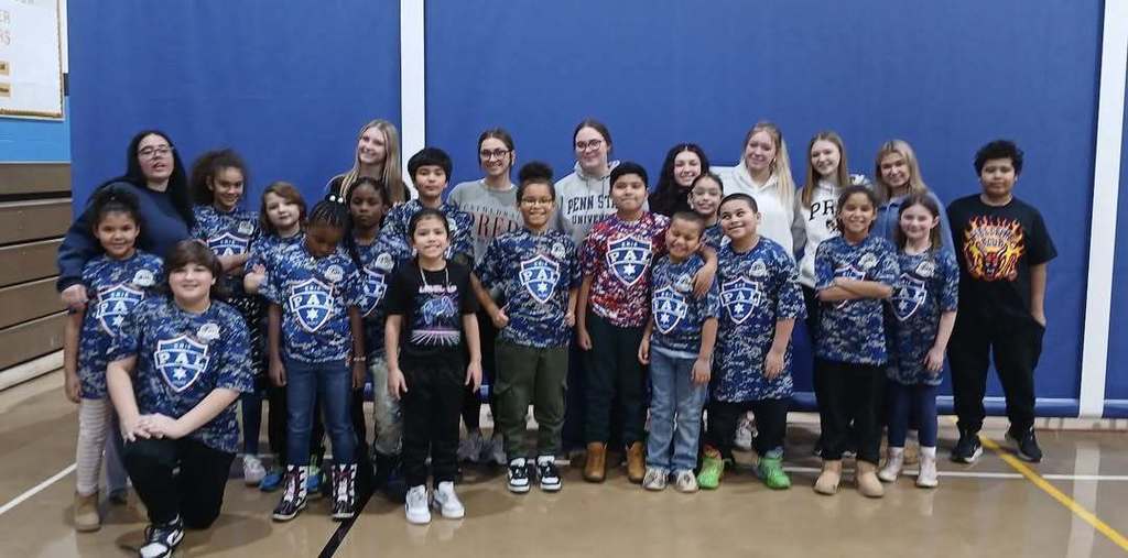 A group of young children in matching shirts and seven young ladies smiling.