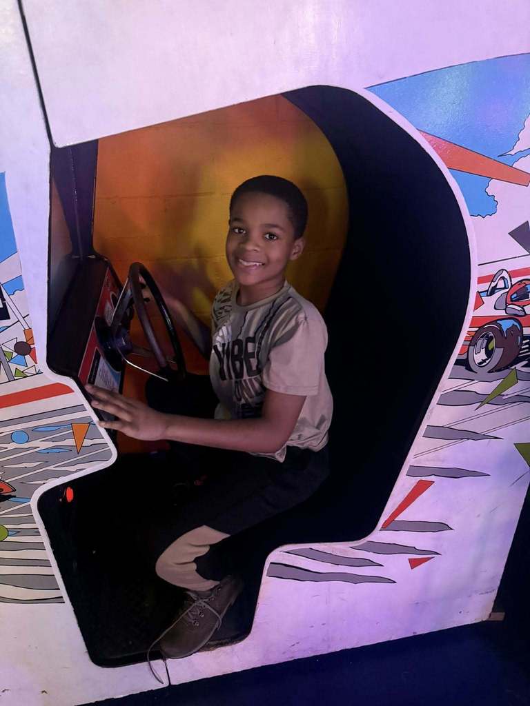 Young boy sitting inside a racing game booth.