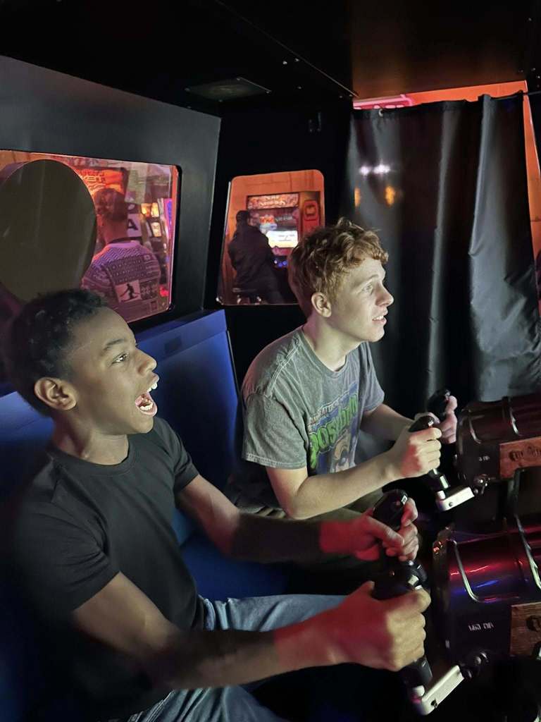 Two young boys playing a racing game at an arcade room.