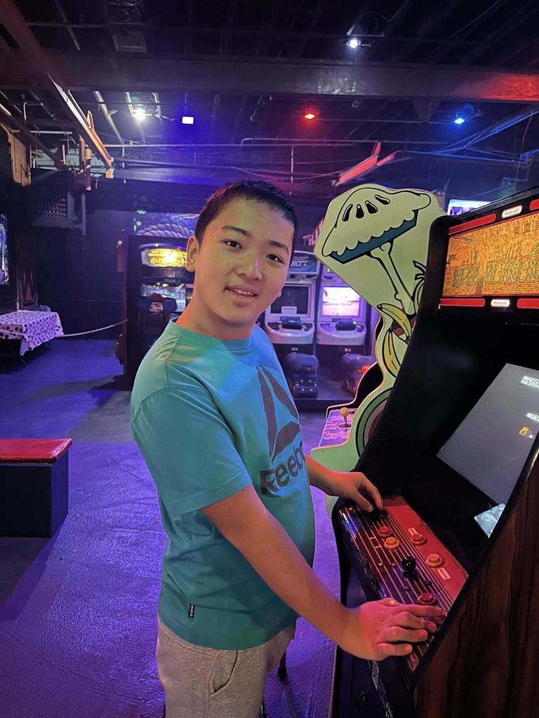 Young boy in a blue shirt smiling at an arcade game. 