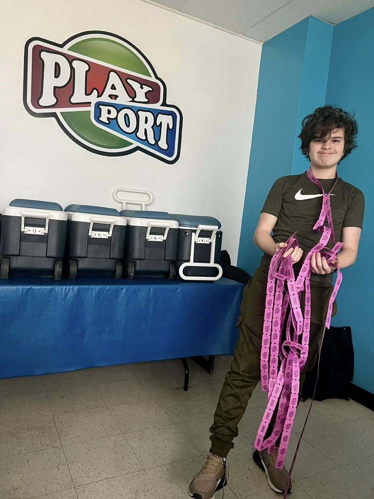 Young boy holding a lot of pink tickets in his hands and around his neck. 