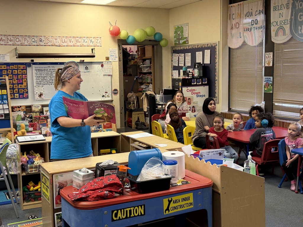 Women reading a book to a classroom of small kids. 