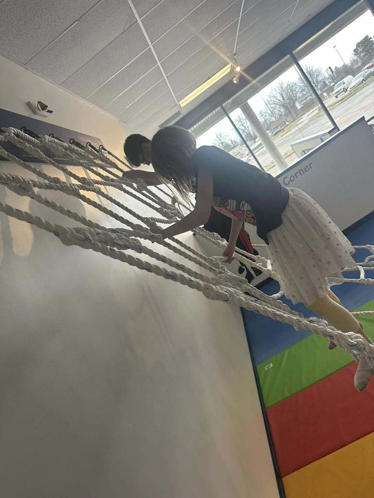 Kids climbing an obstacle rope at a gym.