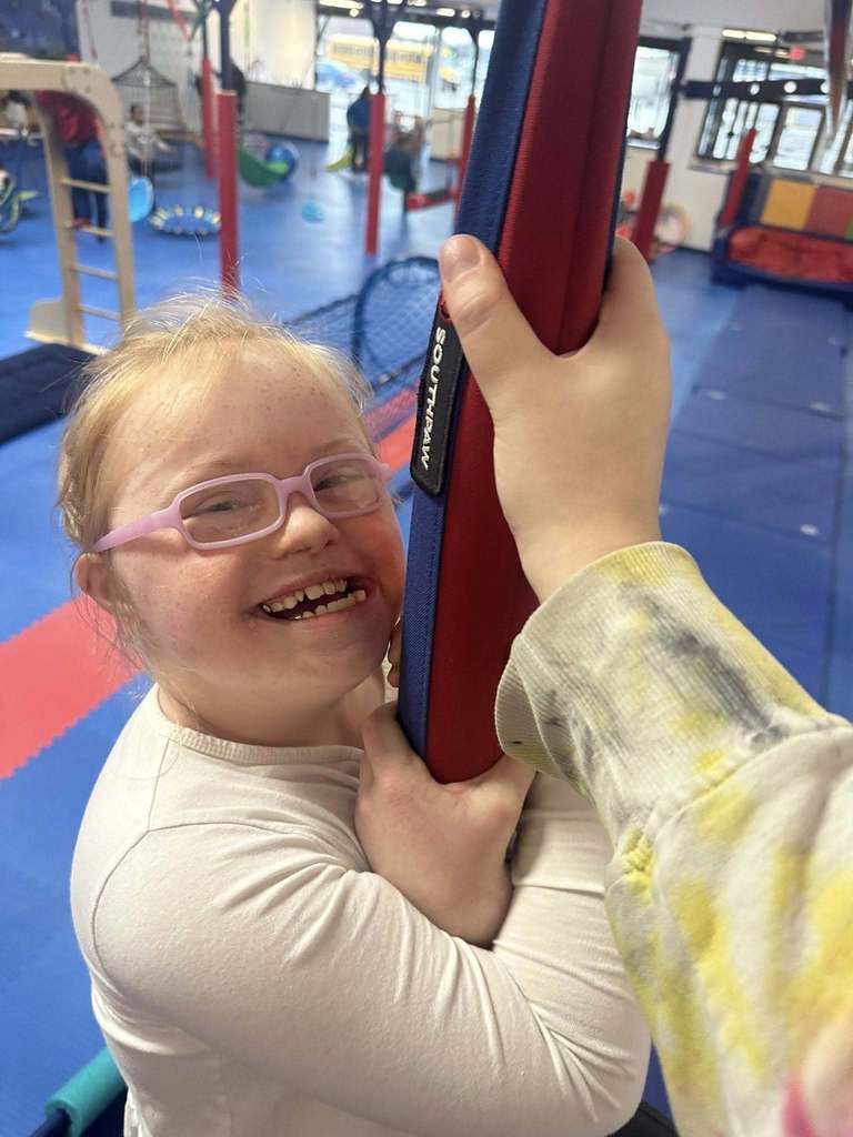 Young girl with pink glasses smiling.