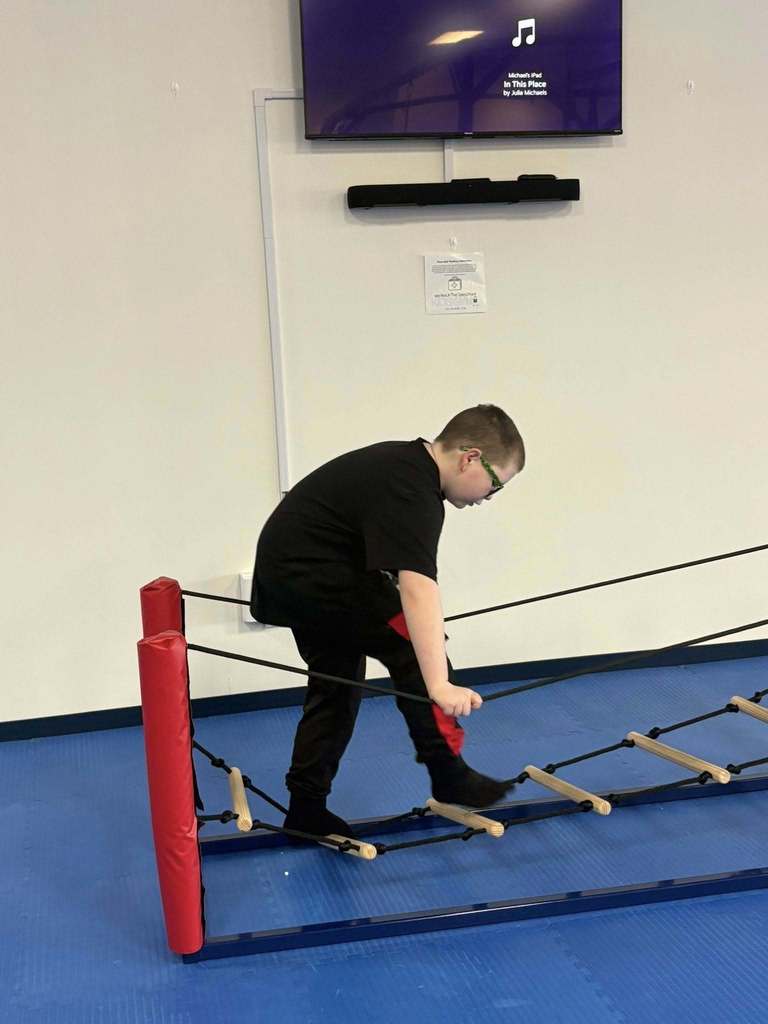 A young boy dressed in black walking an obstacle at a gym.