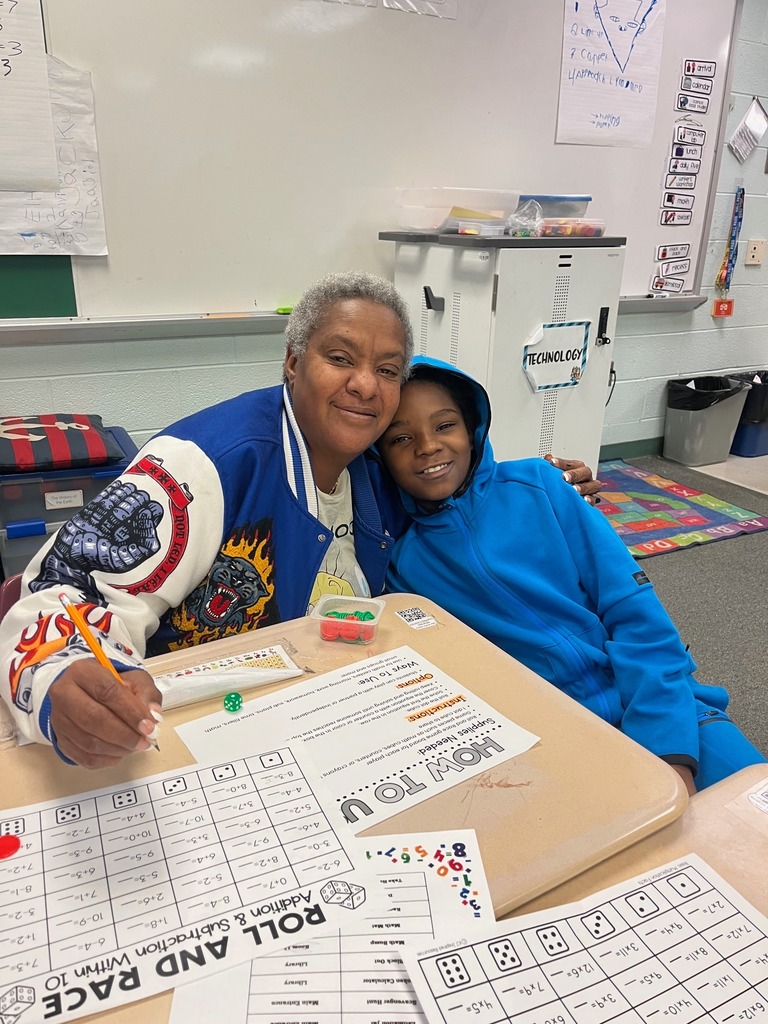 A women hugging a child in a blue hoodie while they play a math game in a classroom.