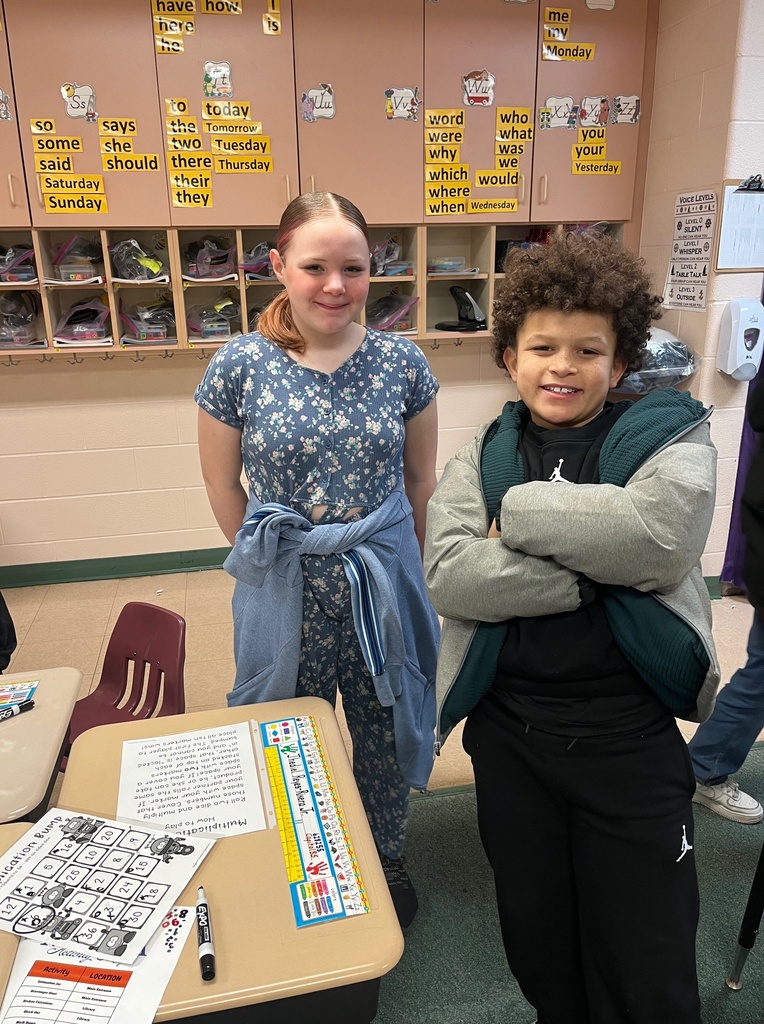 Young girl and young boy standing and smiling in a classroom.