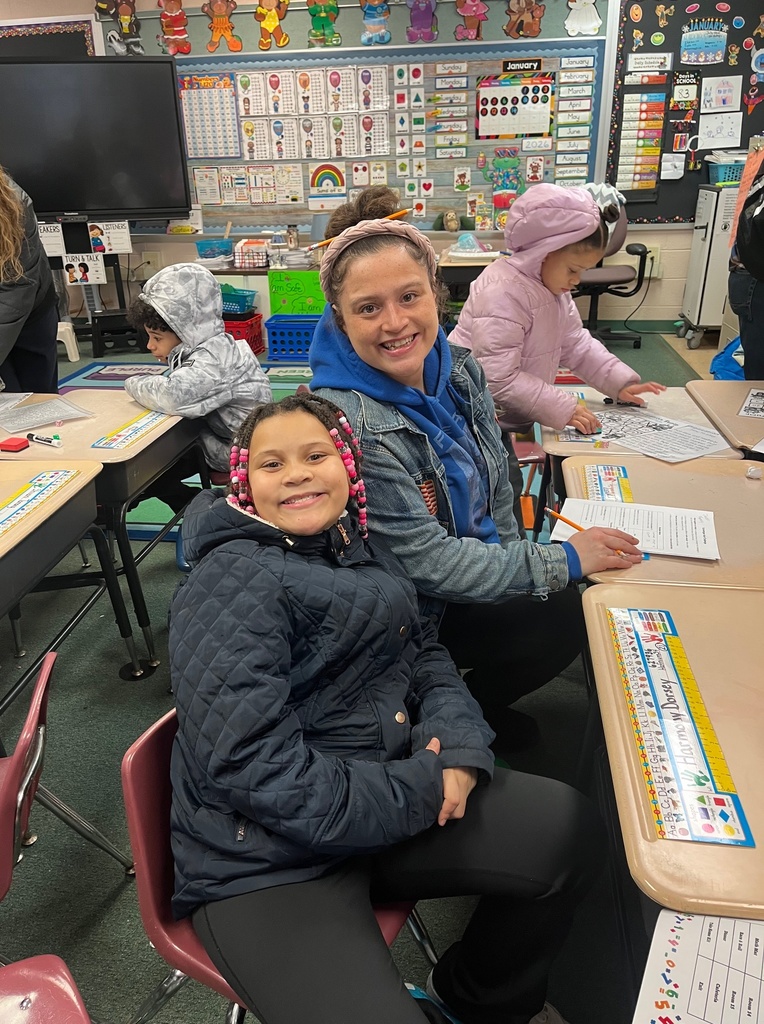 Young girl smiling next to an adult female while sitting in a classroom.
