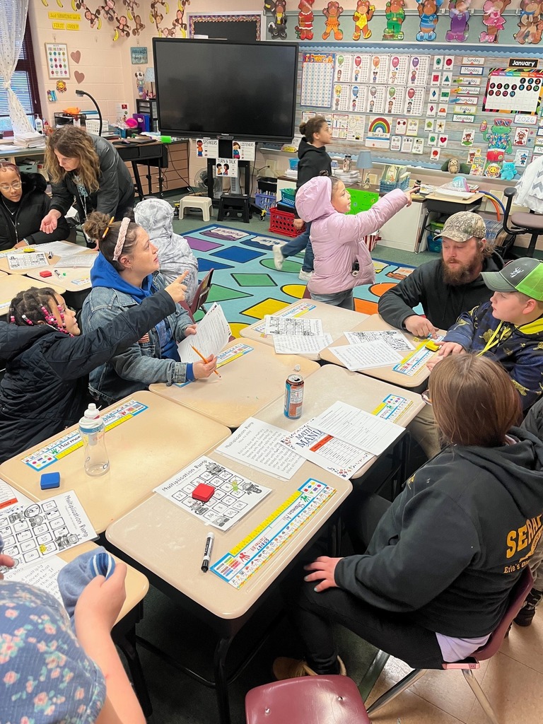 Children and adults gathered around school desks and playing games.