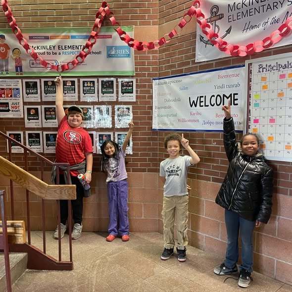 Kids standing in a hall and pointing up at a red paper chain. 