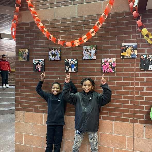 Kids standing in a hall and pointing up at a red and orange paper chain. 