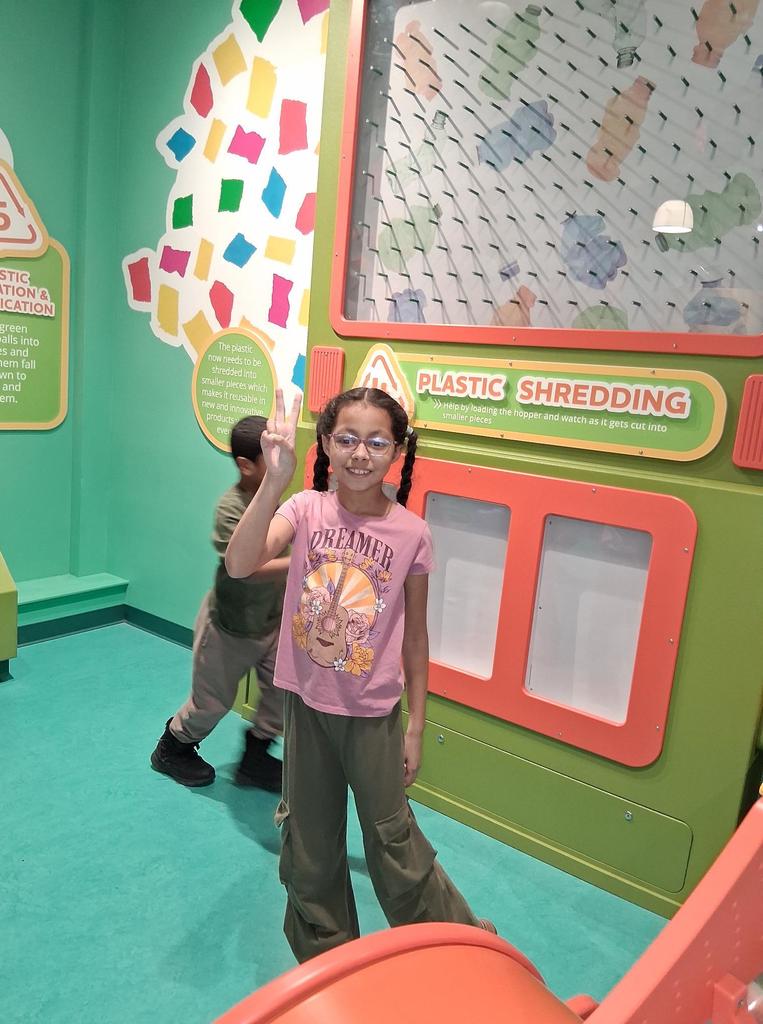 Young girl in a pink shirt and glasses holding two fingers up and smiling. 