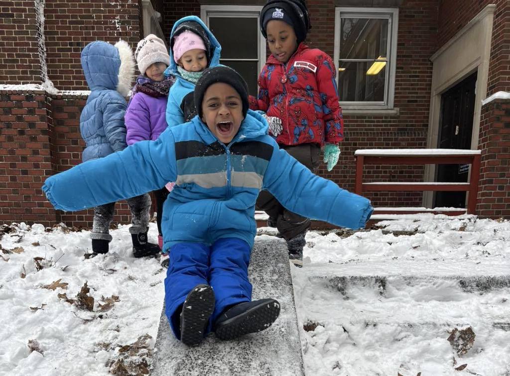 Young boy in a blue winter jacket sliding down a slide in the snow. 