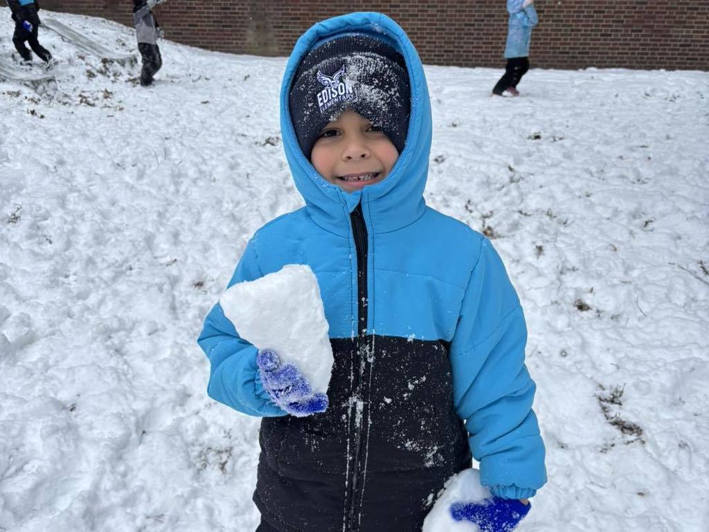 Young boy in a blue winter jacket standing outside and holding snow in his hands. 