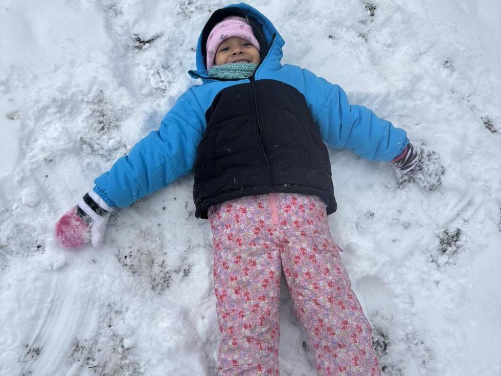 Young child in a blue winter coat making a snow angel. 