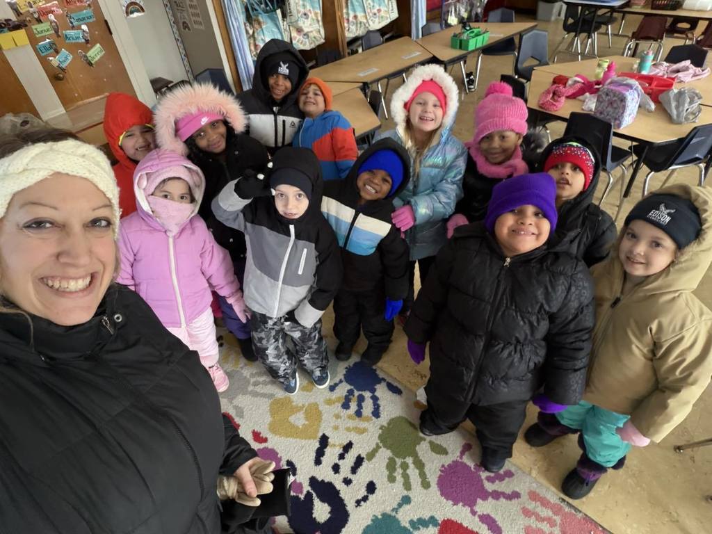 Teacher and students in a classroom and dressed in winter jackets, hats, and gloves.