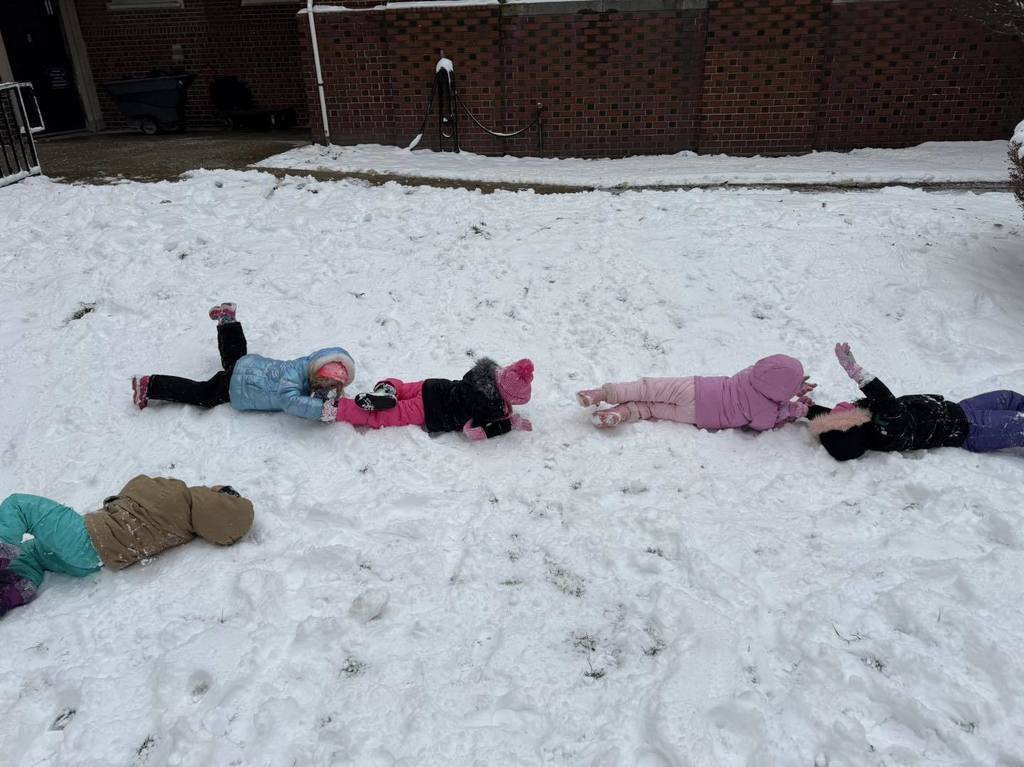 Kids laying on the ground playing in the snow. 