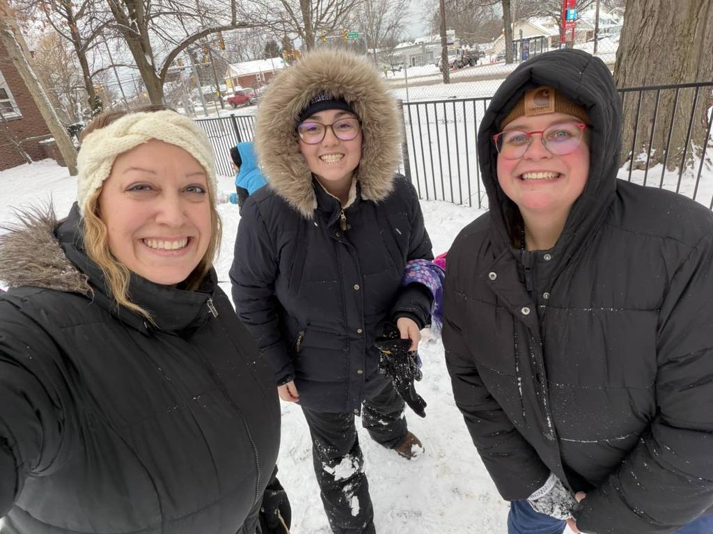 Three adults in black jackets smiling outside in the snow.