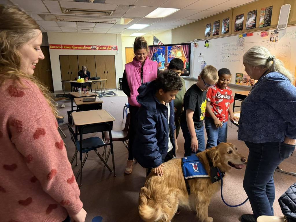 Kids petting a golden retriever dog in a classroom. 