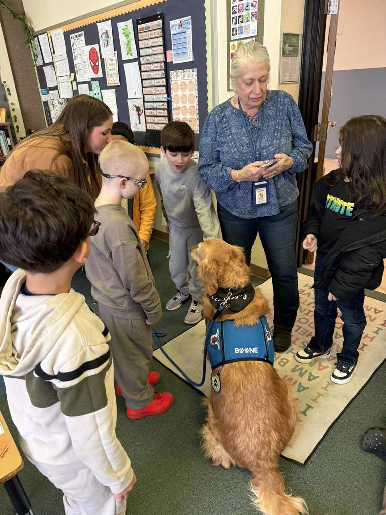 Kids and adults huddled around a golden retriever dog. 