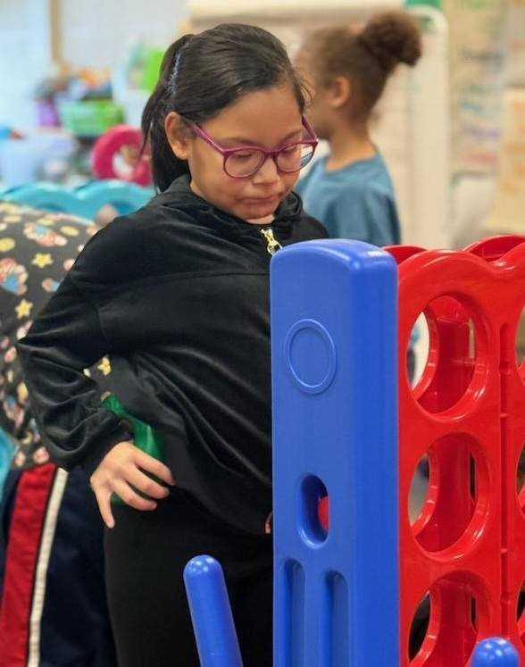 Young girl in pink glasses standing.